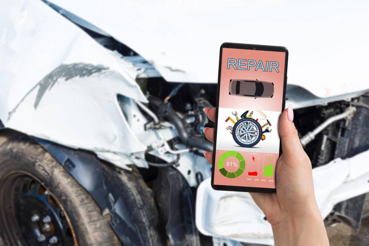 A person holds a smartphone displaying a car repair app near a damaged vehicle, showing repair progress and tools.