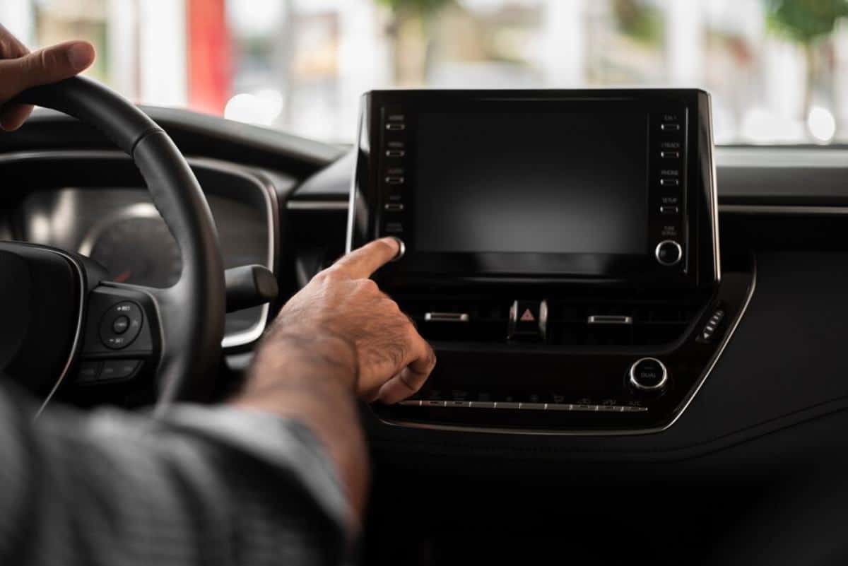 A hand adjusts the touchscreen controls of a modern car's dashboard, with a blurred steering wheel in the foreground.