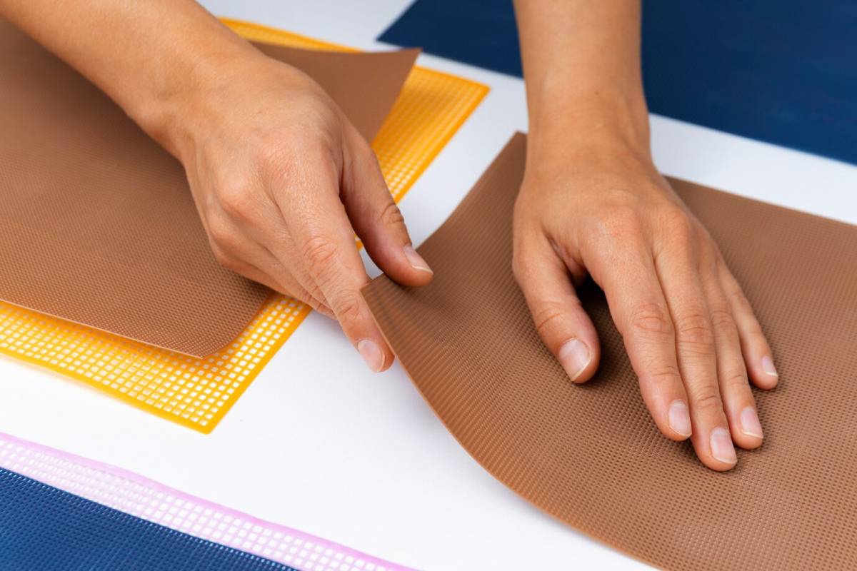 Hands peeling off a corner of adhesive non-slip fabric on a white surface.