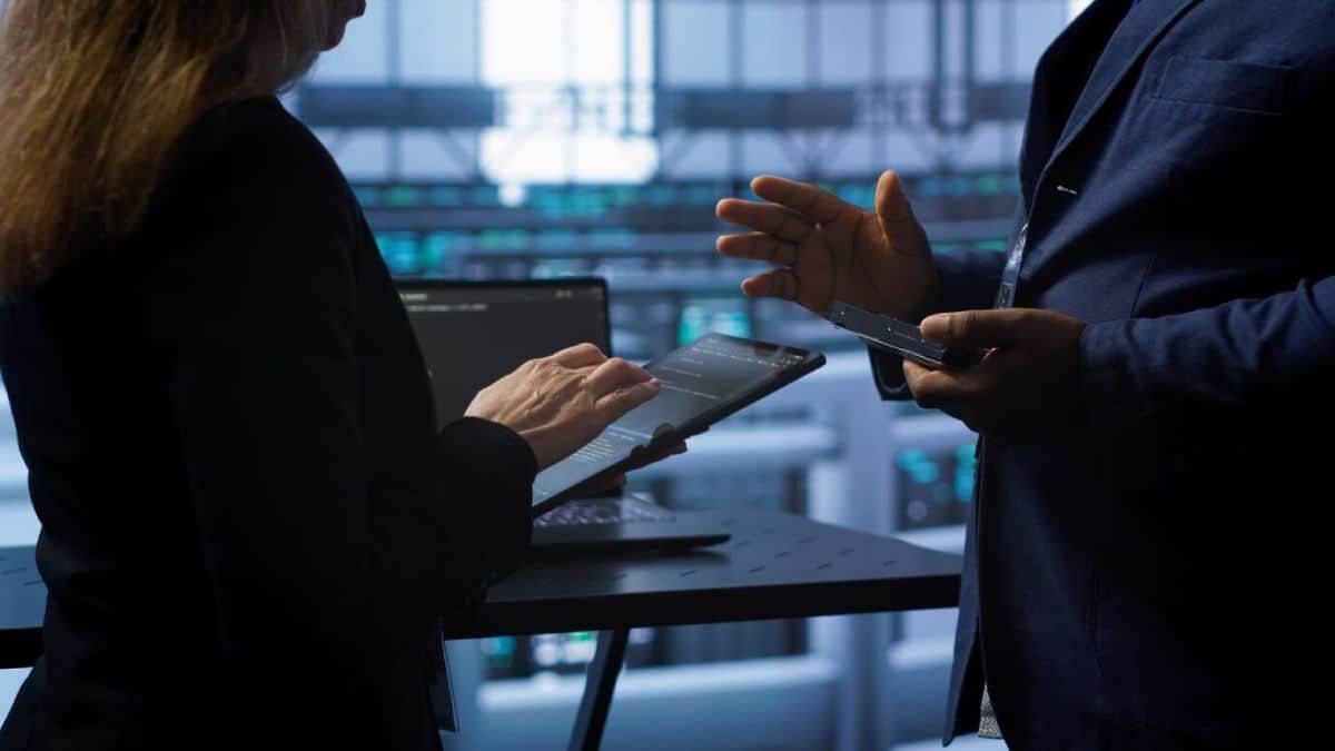 Two professionals engage in a discussion, using a tablet and smartphone